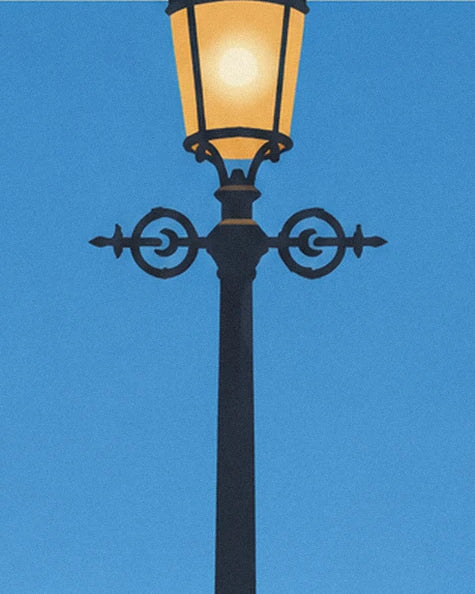 Eine schwarze Straßenlaterne mit verzierten Schnörkeln und einer goldenen Laterne vor blauem Hintergrund