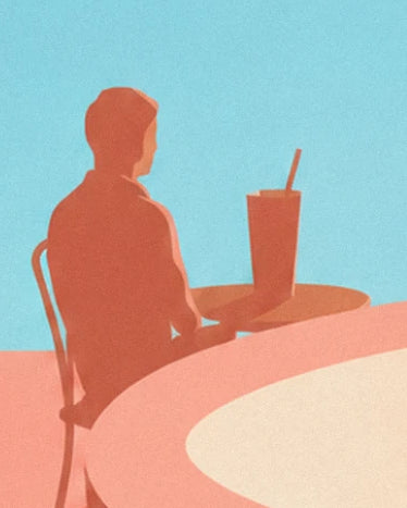 Un homme de dos sur sa chaise de café, face à son verre posé sur la table de la terrasse