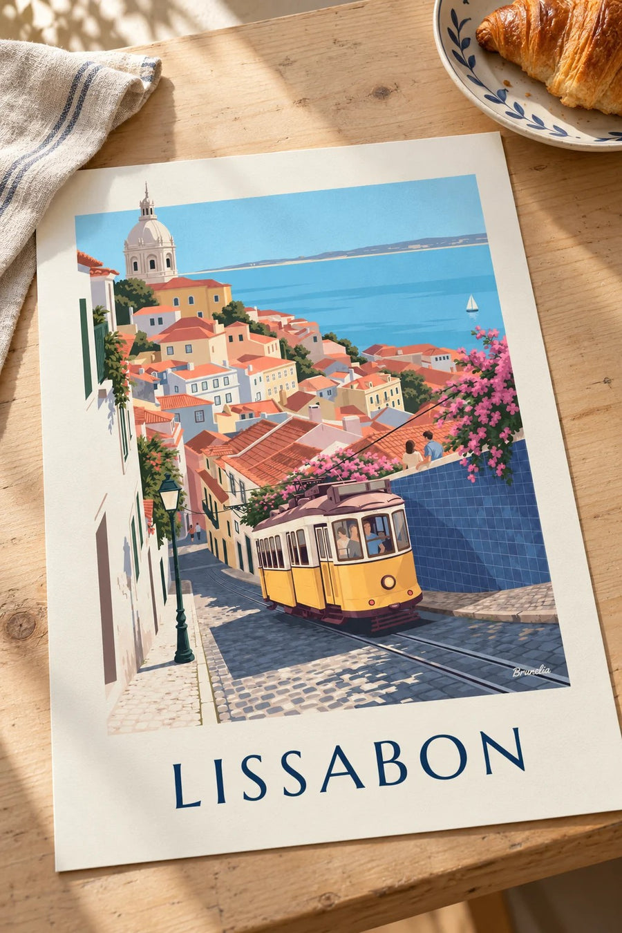 Poster gelbe Straßenbahn in einer Kopfsteinpflastergasse in Lissabon mit Blick auf den Tejo: flach auf einem Tisch